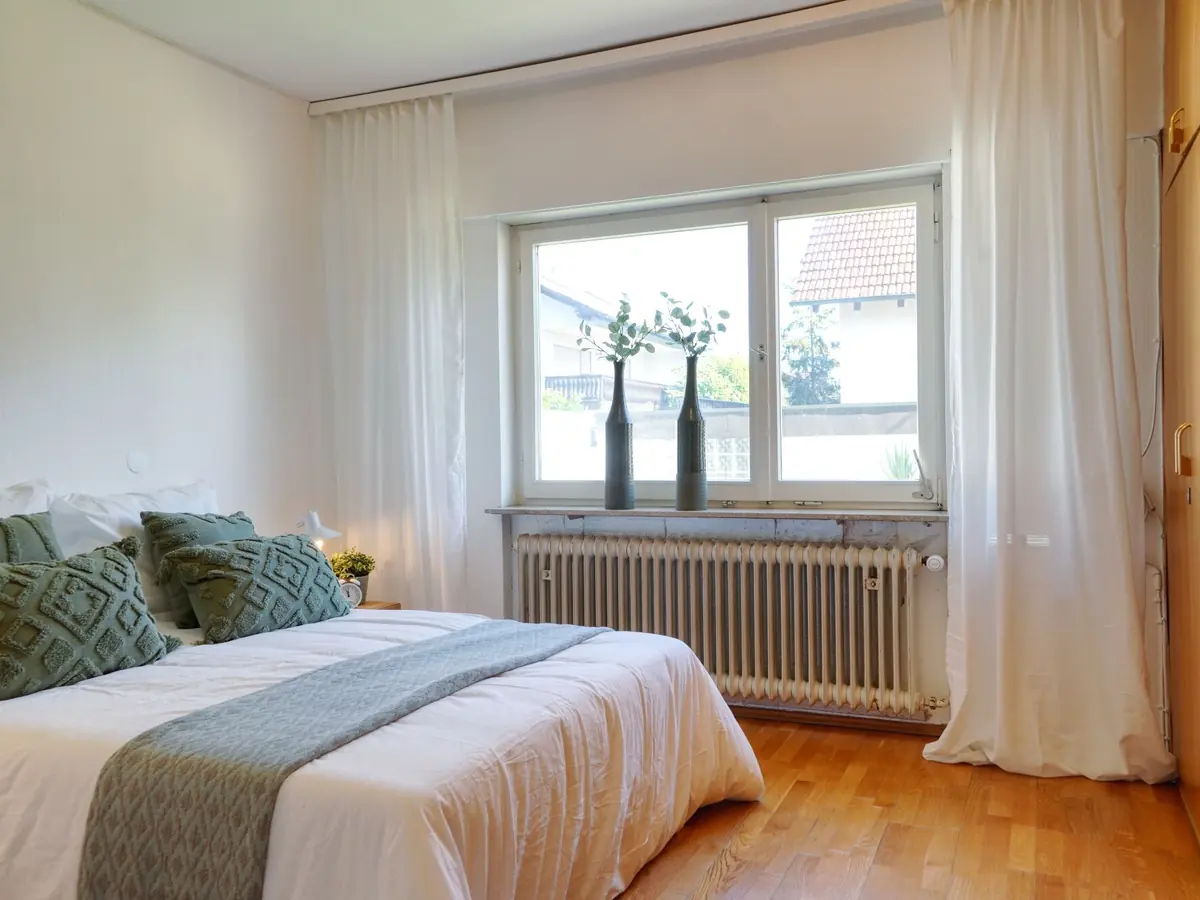 Nachher: helles Schlafzimmer mit gemachtem Bett und Vorhängen